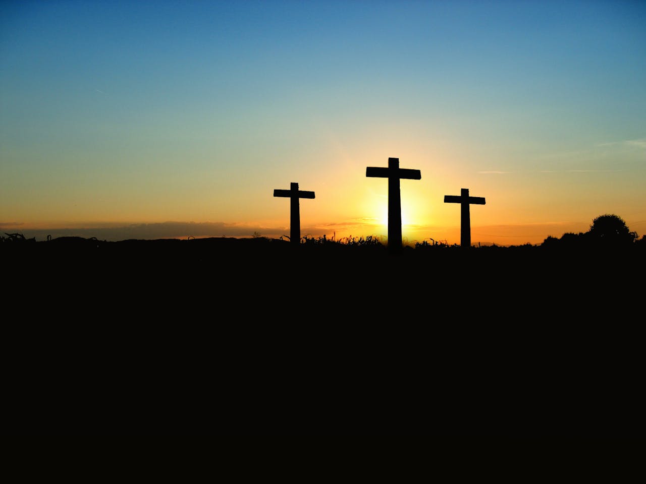 about-03 Silhouette of three crosses against a vibrant sunset sky.