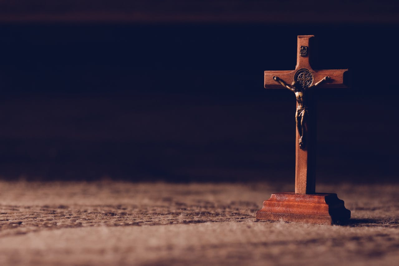 about-04 A solitary wooden crucifix stands on a carpet, casting a shadow in dim ambient lighting symbolizing peace and reflection.