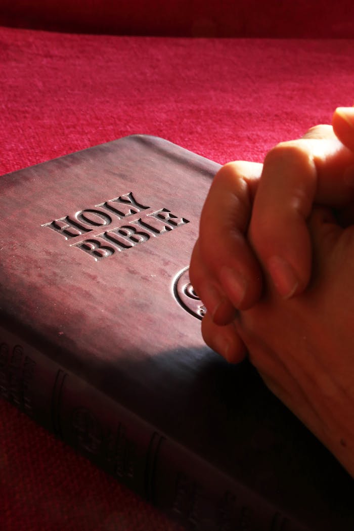 services-02 Close-up of hands praying on a Holy Bible, symbolizing faith and spirituality.